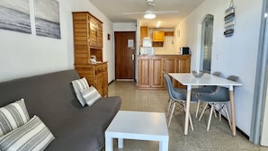Un espacio habitable compacto con sofá, una mesa de comedor y una kitchenette al fondo.