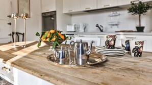 Un comptoir de cuisine sur lequel se trouve un plateau avec une théière, un sucrier et un bol de fruits. On y voit également des assiettes et des tasses, et une plante en pot à l’arrière-plan.