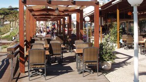 Un café en plein air doté de pergolas en bois, de chaises et de tables en osier.