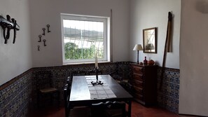 Un coin repas avec une table dressée pour quatre personnes, une fenêtre donnant sur un paysage verdoyant, un porte-clés fixé au mur et un meuble en bois avec une lampe.