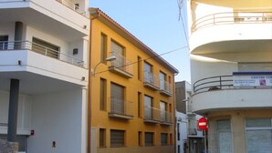 A street view with a yellow building, a white building with balconies, and a sign for a medical center. - MESTRAL 1-6 (L'Escala)