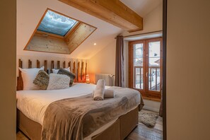 A bedroom with a sloped ceiling, a skylight, a large bed with multiple pillows, a radiator, and a view of the outside through a window.