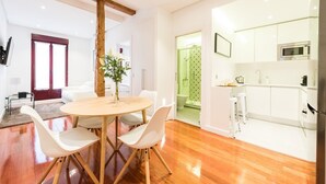 Une cuisine moderne avec des meubles blancs, un four à micro-ondes et un évier. On y trouve également un coin repas avec une table ronde et des chaises blanches.