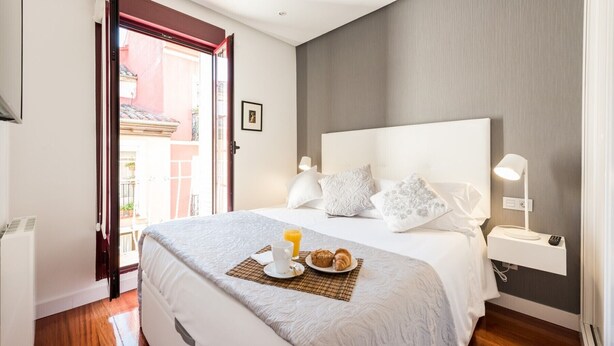 Un lit bien fait, avec un plateau de petit-déjeuner, une table de chevet avec une lampe, et une vue sur l’extérieur par une porte ouverte.