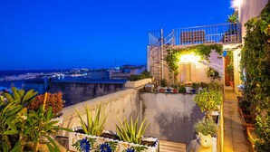 Una terraza en la azotea con plantas en macetas, una escalera y vista a la ciudad al anochecer.
