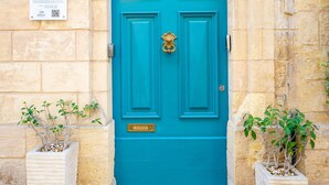 Una puerta turquesa con un llamador de bronce, flanqueada por dos macetas con plantas y un letrero encima de la puerta.