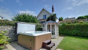 Een bubbelbad, een pergola en een huis met schoorsteen in een achtertuin.