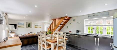 Une cuisine moderne avec un coin repas, un escalier et une vue sur la verdure environnante.