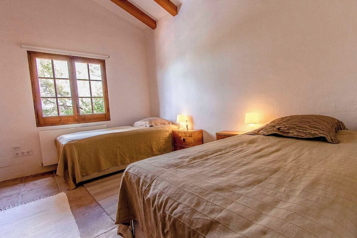 A bedroom with two beds, a window, and a nightstand with a lamp.