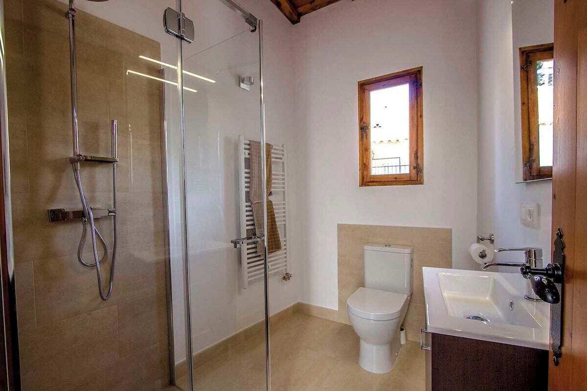 A bathroom with a glass shower enclosure, a toilet, and a sink with a mirror.