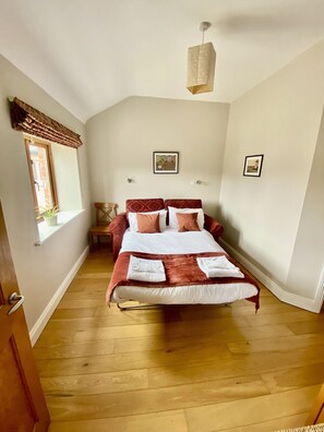 A bedroom with a bed, a window, a chair, and a wall-mounted light fixture. - Two bedroomed cottage in a landscaped courtyard  in the heart of  Ireland's Ancient East region. (Navan)