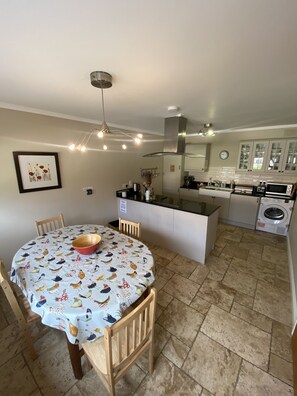 A kitchen with a dining area, featuring a round table with chairs, a hanging light fixture, and a built-in oven. - Two bedroomed cottage in a landscaped courtyard  in the heart of  Ireland's Ancient East region. (Navan)