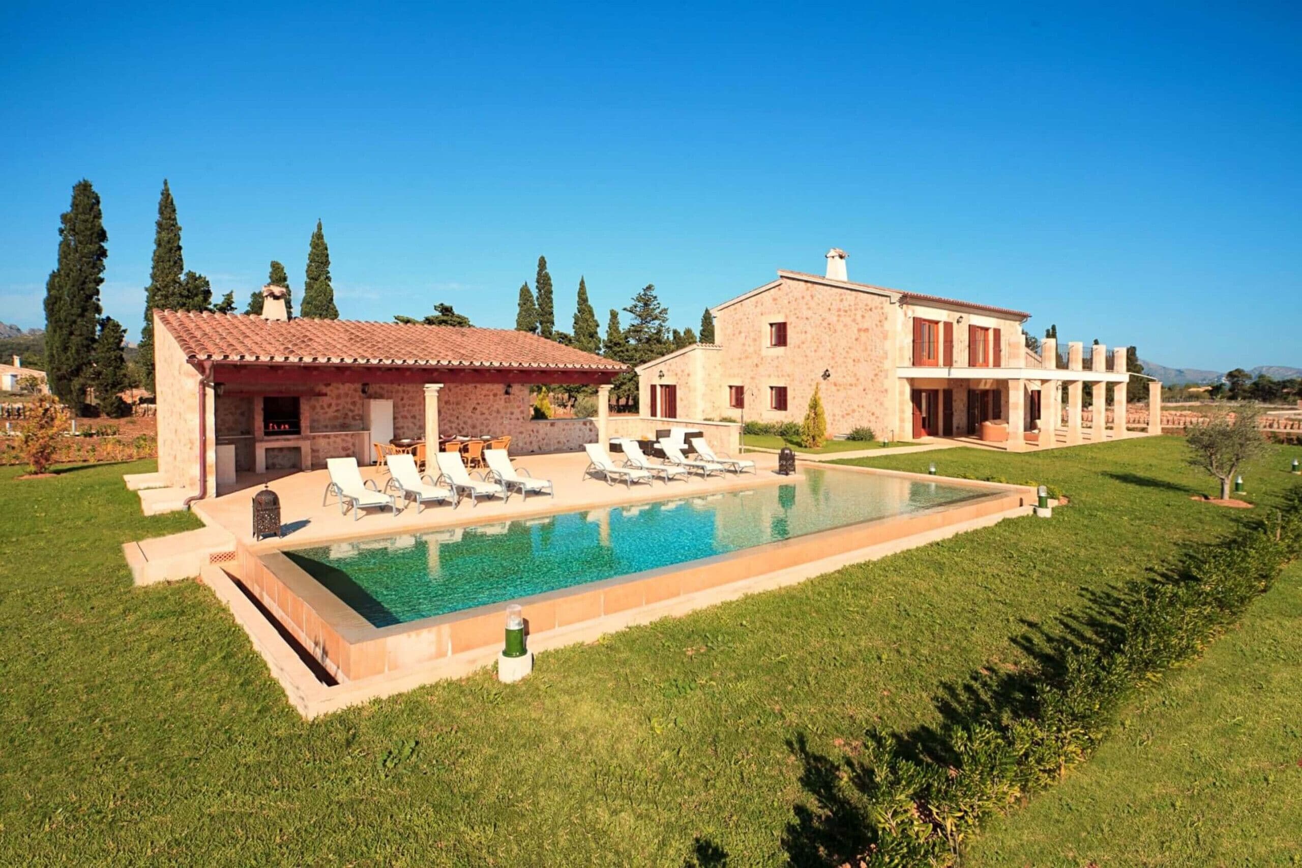 A large house with a swimming pool, multiple lounge chairs, and a well-maintained lawn.