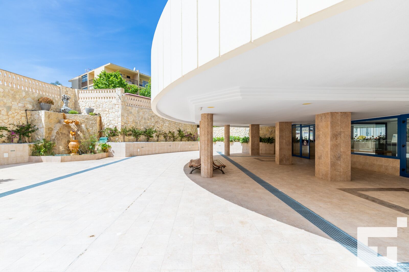 Un vaste espace extérieur agrémenté d’une fontaine, de murs en pierre et d’un bâtiment moderne doté de grandes colonnes.