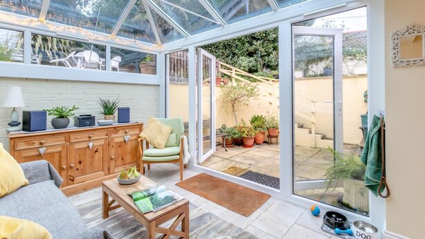 A conservatory with a glass ceiling, wooden furniture, a sofa, a table, and potted plants. - 2 Bed in Appledore (oc-drum) (Appledore)