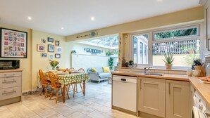 A modern kitchen with a dining area, large windows, and a white brick wall. - 2 Bed in Appledore (oc-drum) (Appledore)