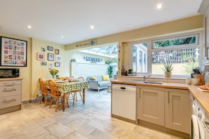 A modern kitchen with a dining area, large windows, and a white brick wall. - 2 Bed in Appledore (oc-drum) (Appledore)