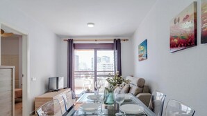 A modern dining area with a glass table, clear chairs, a sofa, and a TV. - Zafiro 35B - Grupo Turis - Calpe, Costa Blanca (Calpe)