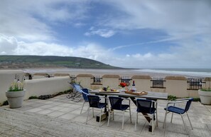 A terrace with a table and chairs overlooking a beach.