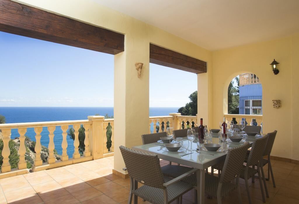 Un comedor con mesa preparada para seis personas, con vistas a un paisaje marino.