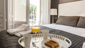 Hotellihuone, jossa on sänky, tarjotinalus, jossa on churroja, lasi appelsiinimehua ja valkoinen muki.