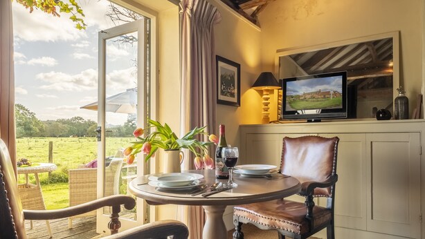 A dining area with a table set for two, a television, and a view of a green landscape.