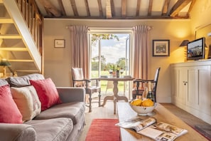 A cozy living room with a grey sofa, a wooden staircase, a dining table with chairs, and a television on a cabinet. - Acorn Cottage, Oulton, Norfolk (Aylsham)