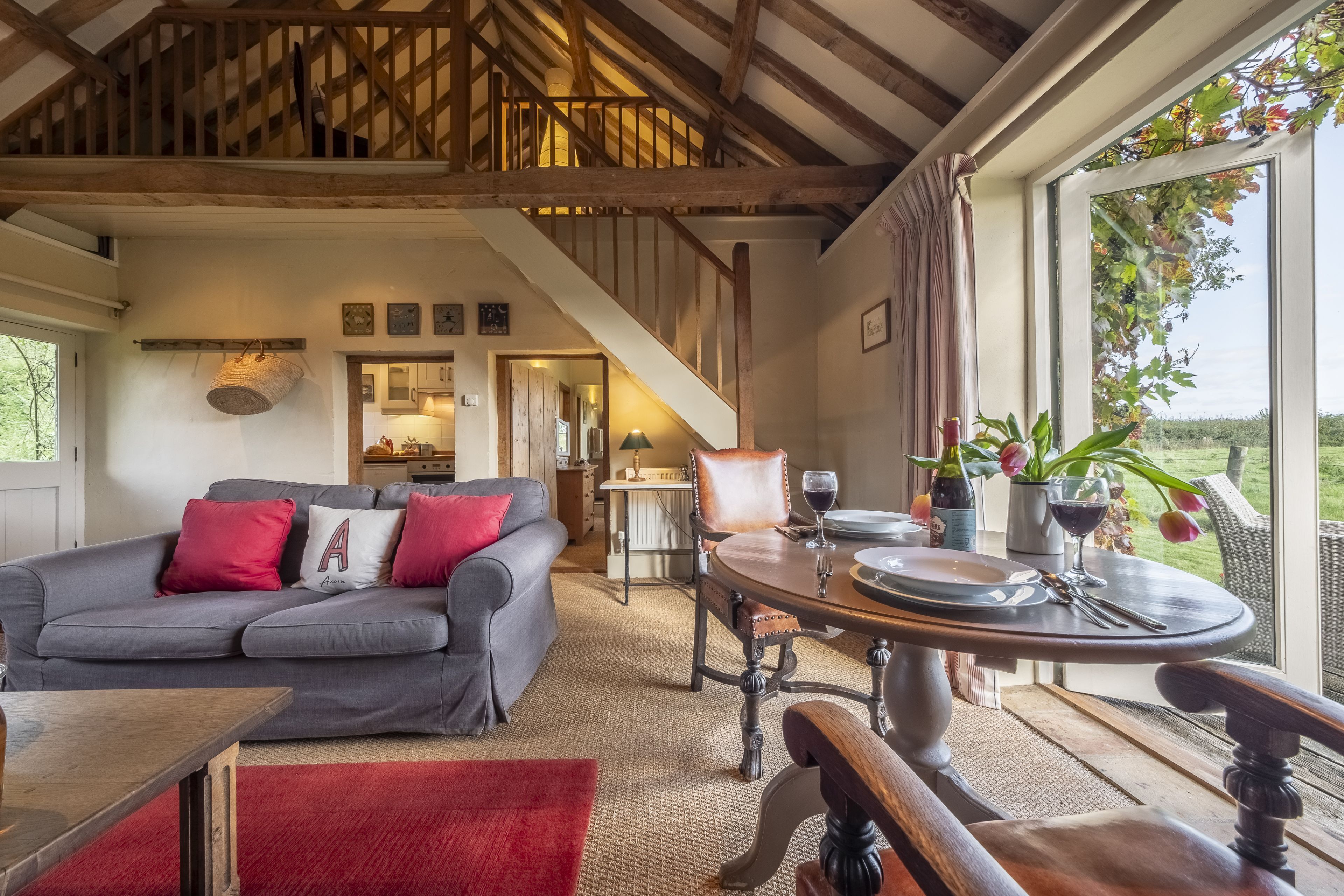 Een ruime woonkamer met een grijze bank, een houten eettafel en uitzicht op het buiten.