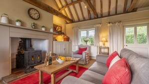 A cozy living room with a fireplace, a sofa, a table with drinks, and a window with curtains.