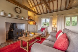 A cozy living room with a fireplace, a sofa, a table with drinks, and a window with curtains.