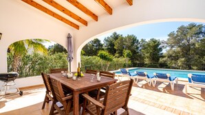 Eine Außenpatio mit Holztisch und -stühlen, einem Grill und einem Poolbereich mit Liegestühlen.