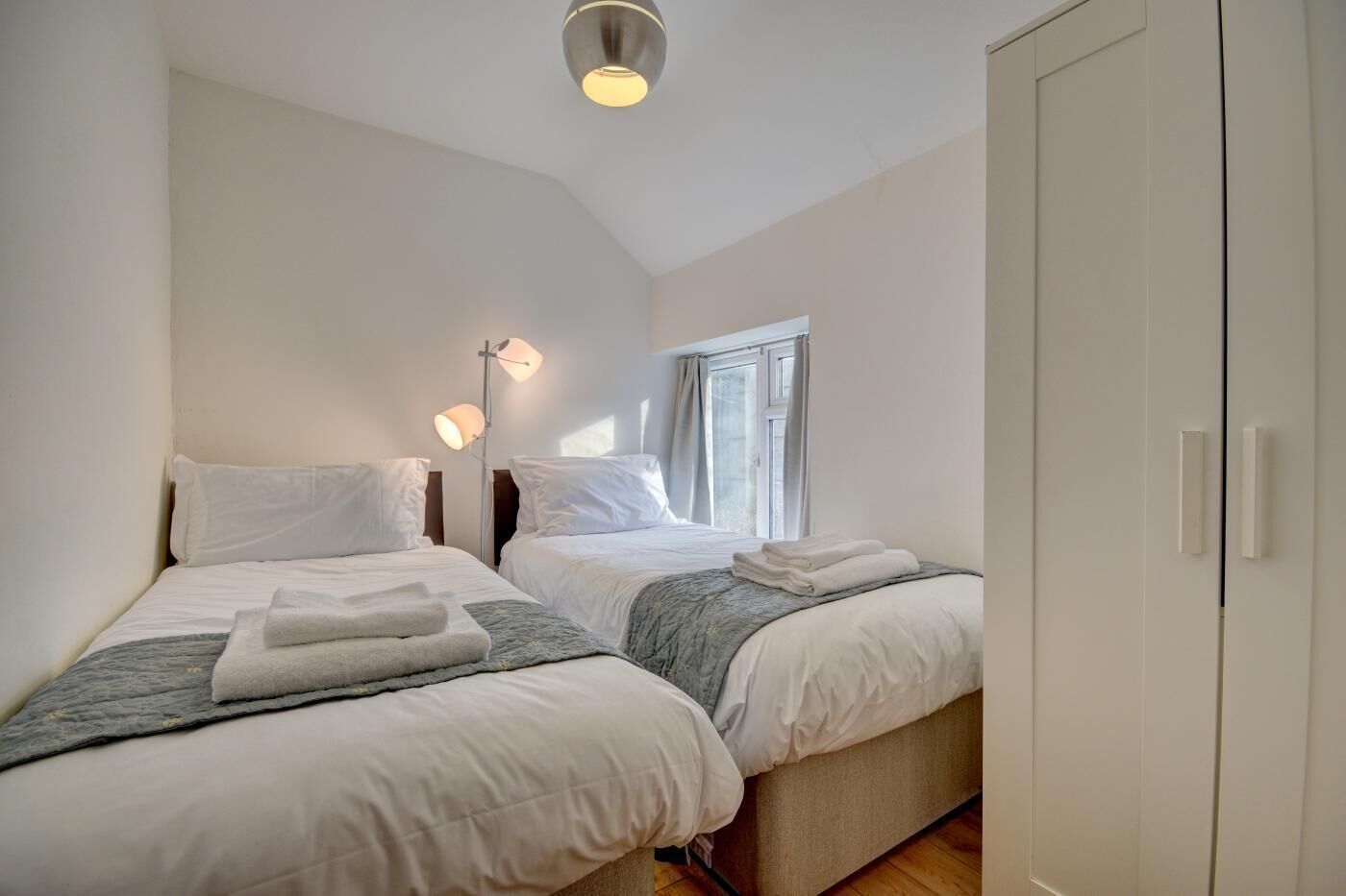 Ein Schlafzimmer mit zwei Betten, einer Nachttischlampe, einem Kleiderschrank und einem Fenster.