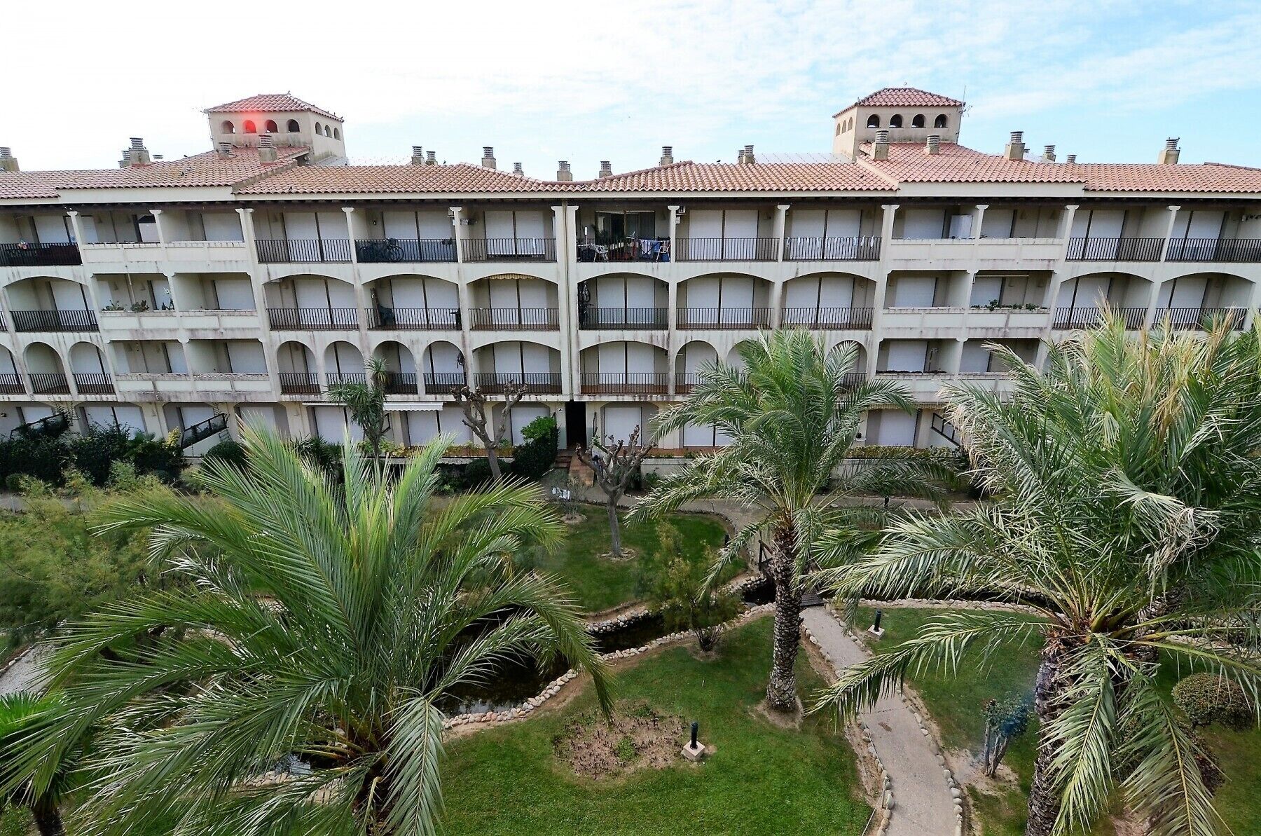 Ein mehrstöckiges Hotel mit Innenhof, der Palmen und einem kleinen Wasserspiel enthält.