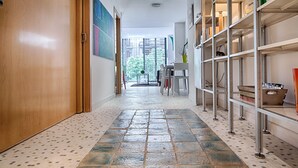 A hallway with a tiled floor, a wooden door, and a metal shelving unit with various items. - Pedrera - Habitat Apartments (Barcelona)