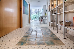 A hallway with a patterned floor, a wooden door, and a shelving unit with various items. - Pedrera - Habitat Apartments (Barcelona)