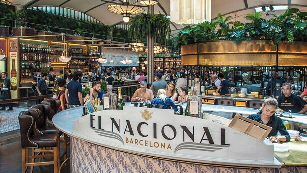 A bustling bar area with a counter labeled "EL NACIONAL BARCELONA," surrounded by patrons and a variety of bottles. - Pedrera - Habitat Apartments (Barcelona)
