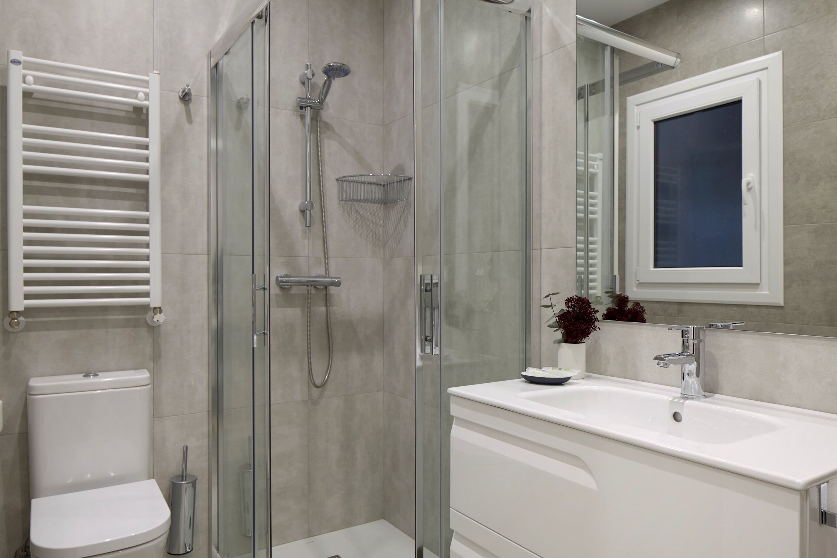 A modern bathroom with a glass-enclosed shower, a white toilet, a sink with a mirror above it, and a towel rack.
