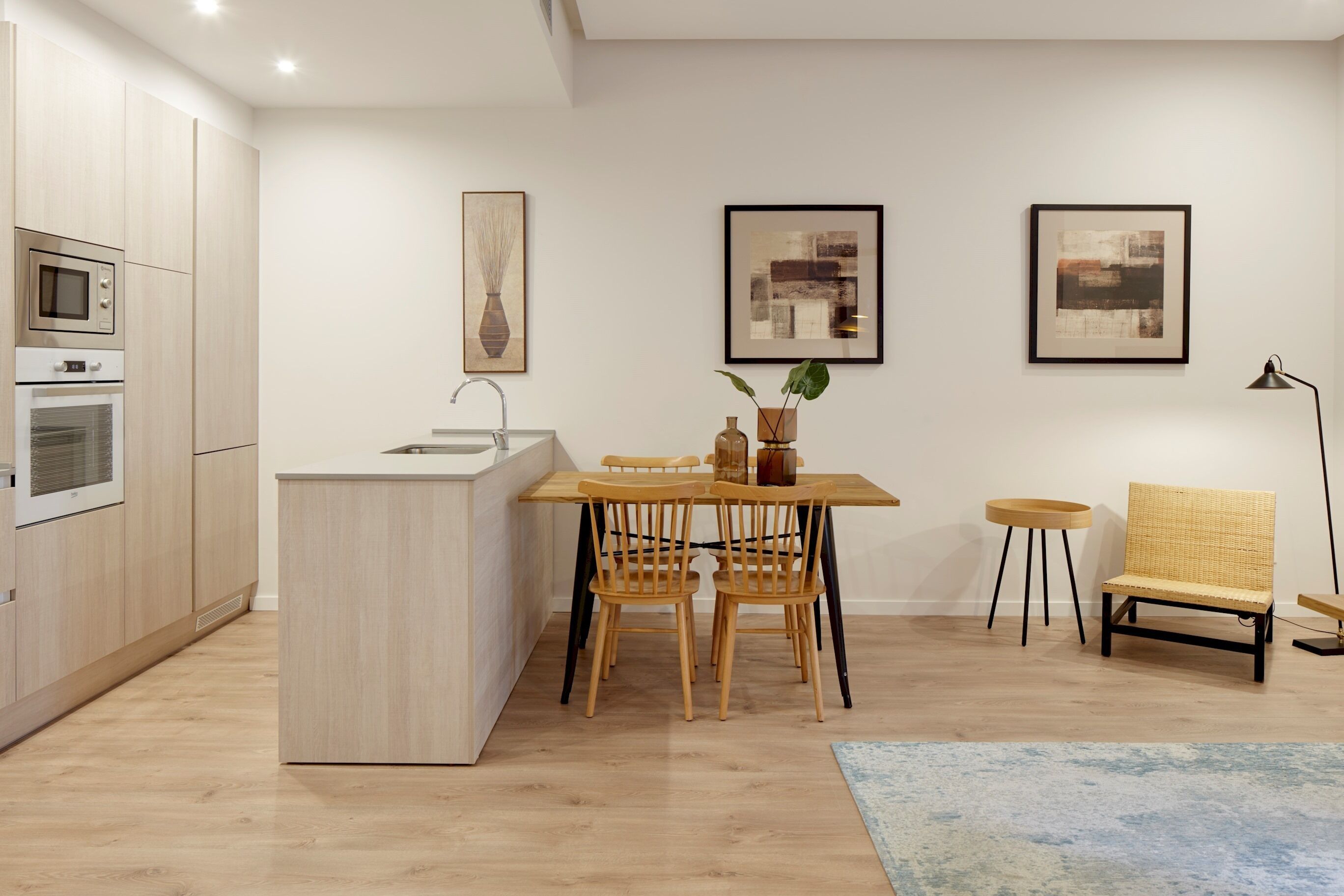 Una cocina moderna con armarios de madera, horno integrado y un comedor con mesa y sillas.