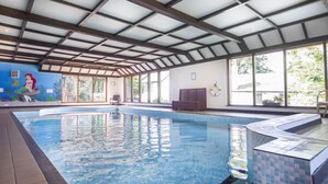 Une piscine intérieure avec des parois en verre transparent, une terrasse carrelée et une fresque murale sur le mur de gauche.