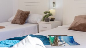 Hotellihuone, jossa on kaksi sänkyä, valkoiset vuodevaatteet ja yöpöytä, jossa on lamppu ja pieni kasvi.