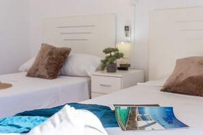 Une chambre d’hôtel avec deux lits, du linge de lit blanc et une table de chevet avec une lampe et une petite plante.