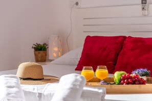En pænt redt seng med en rød pude, en stråhat, to glas appelsinjuice og et fad med frugt og en lille plante.