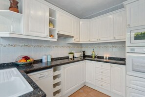 A kitchen with white cabinetry, a granite countertop, a dish rack, a fruit bowl, a toaster, and a microwave.