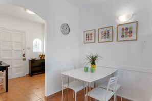 A dining area with a white table, chairs, a clock, and framed artwork on the wall.