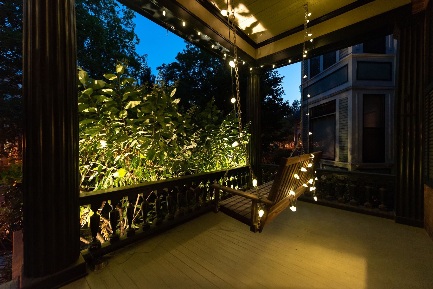 Eine Veranda mit einer Schaukel, umgeben von Pflanzen und Lichterketten.