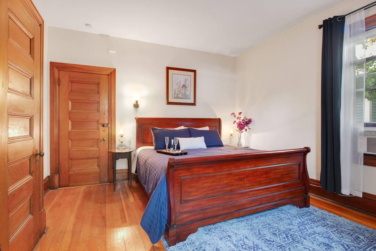 Quarto com cama de madeira, mesa de cabeceira, quadro na parede e janela com cortinas.