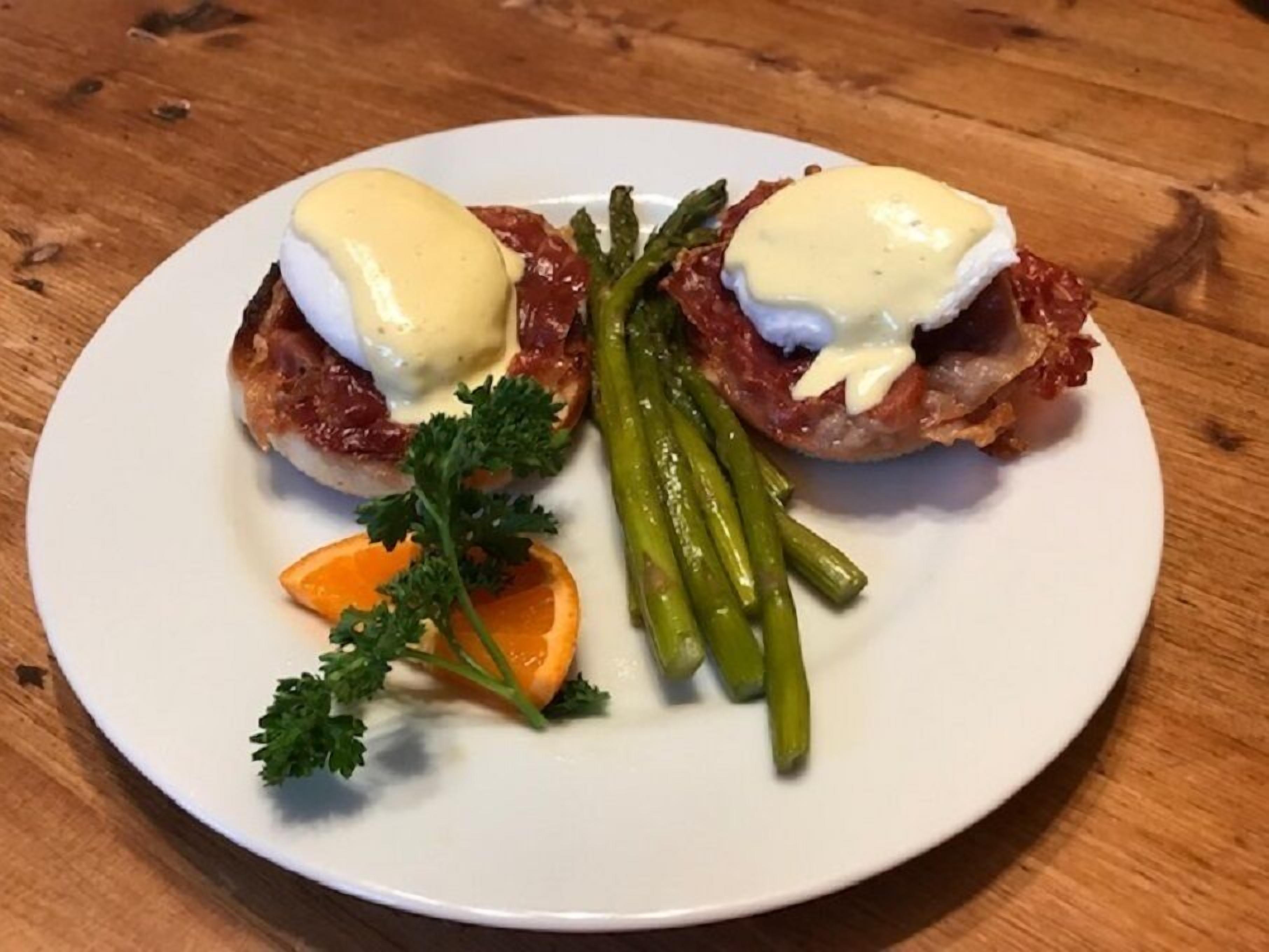 Un plato con dos huevos benedictinos, espárragos y una guarnición de perejil y una rodaja de naranja.
