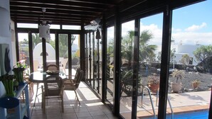 A covered patio with a pool, outdoor furniture, and potted plants.