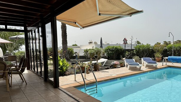 A pool area with lounge chairs and a table, surrounded by potted plants and a view of the cityscape.