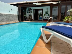 Una piscina con una silla de descanso blanca y un deck con baldosas.